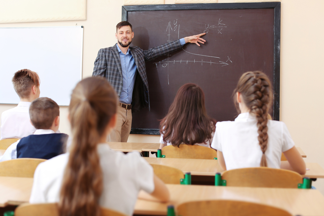 male teacher in a classroom pointing at a blackboard
