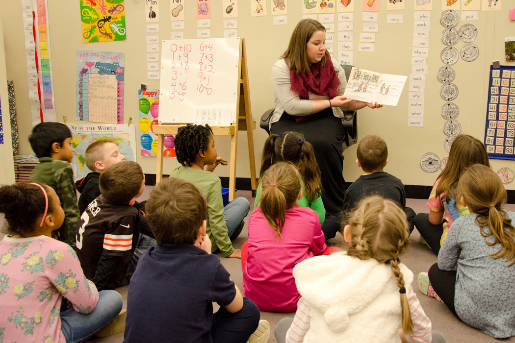 female teaching student reading to a class of young children