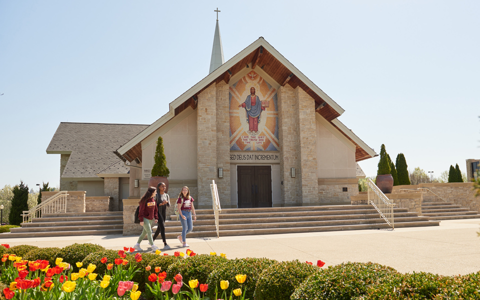 photo of three female students walking in front of Our Lady of Perpetual Help Chapel