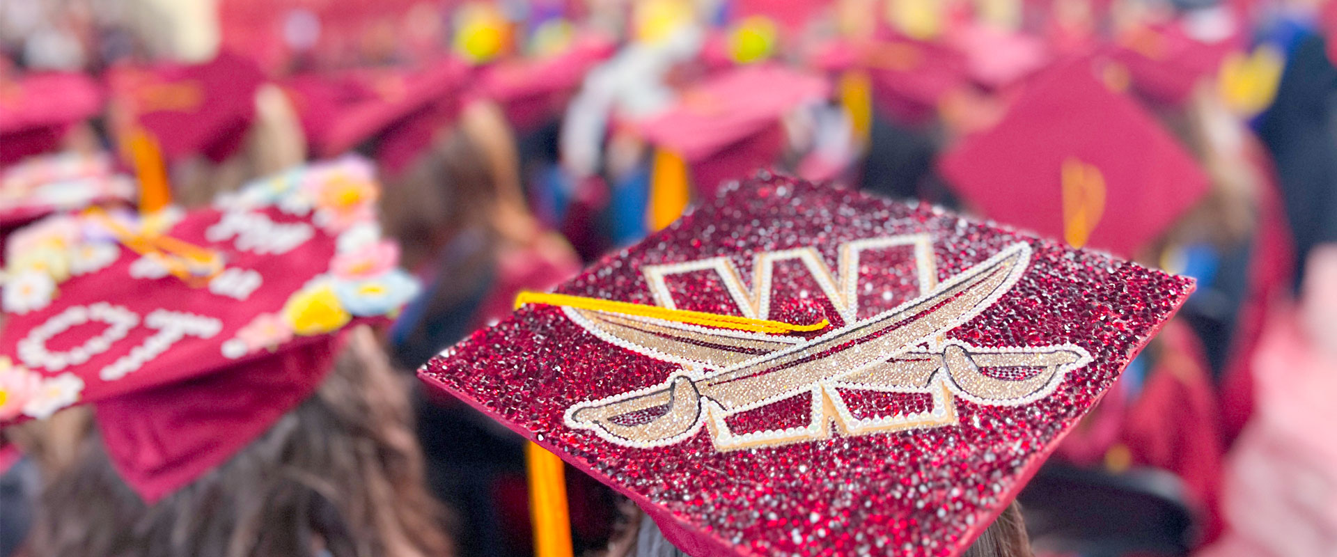 Graduation cap decorated with Walsh's logo, with graduates in the crowd behind.