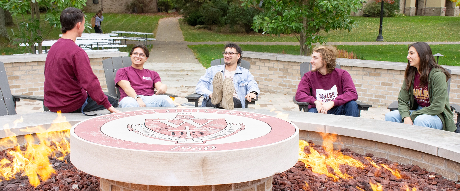 Students engaged in conversation while gathered around a large gas fire pit