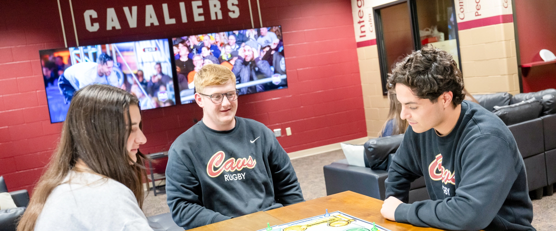 Three students playing a game in the Cavs Den student lounge at Walsh University