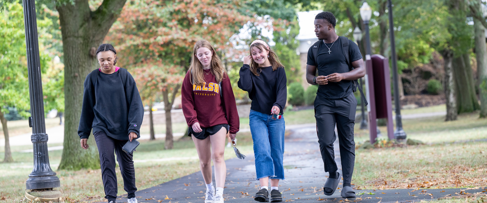 Four students walking towards the viewer using an outdoor sidewalk on the Walsh campus