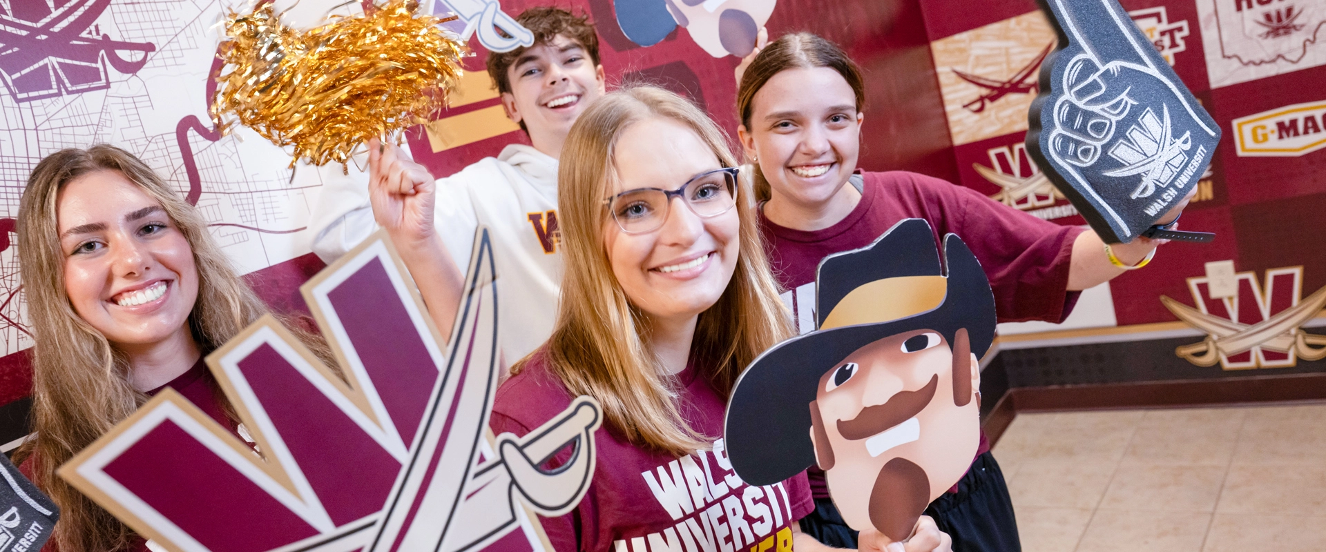 Students clad in Walsh University gear while holding various props depicting Walsh's logos and colors (maroon and gold)