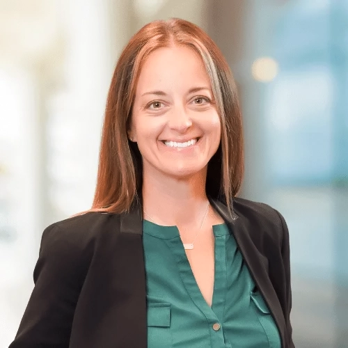 Professional headshot of Annie Yoder, a woman with long brown hair, wearing a green blouse and black blazer, smiling confidently.