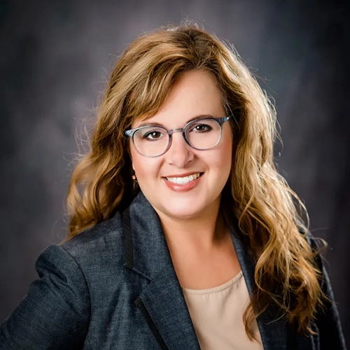Professional headshot of Kimberly Jarvis, a woman with wavy hair, wearing glasses and a business suit, smiling confidently.