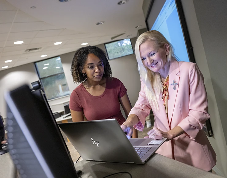A student and faculty member looking at a computer screen and smiling