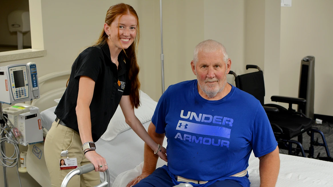 An occupational therapy student helps an elderly client out of bed with the aid of a walker.