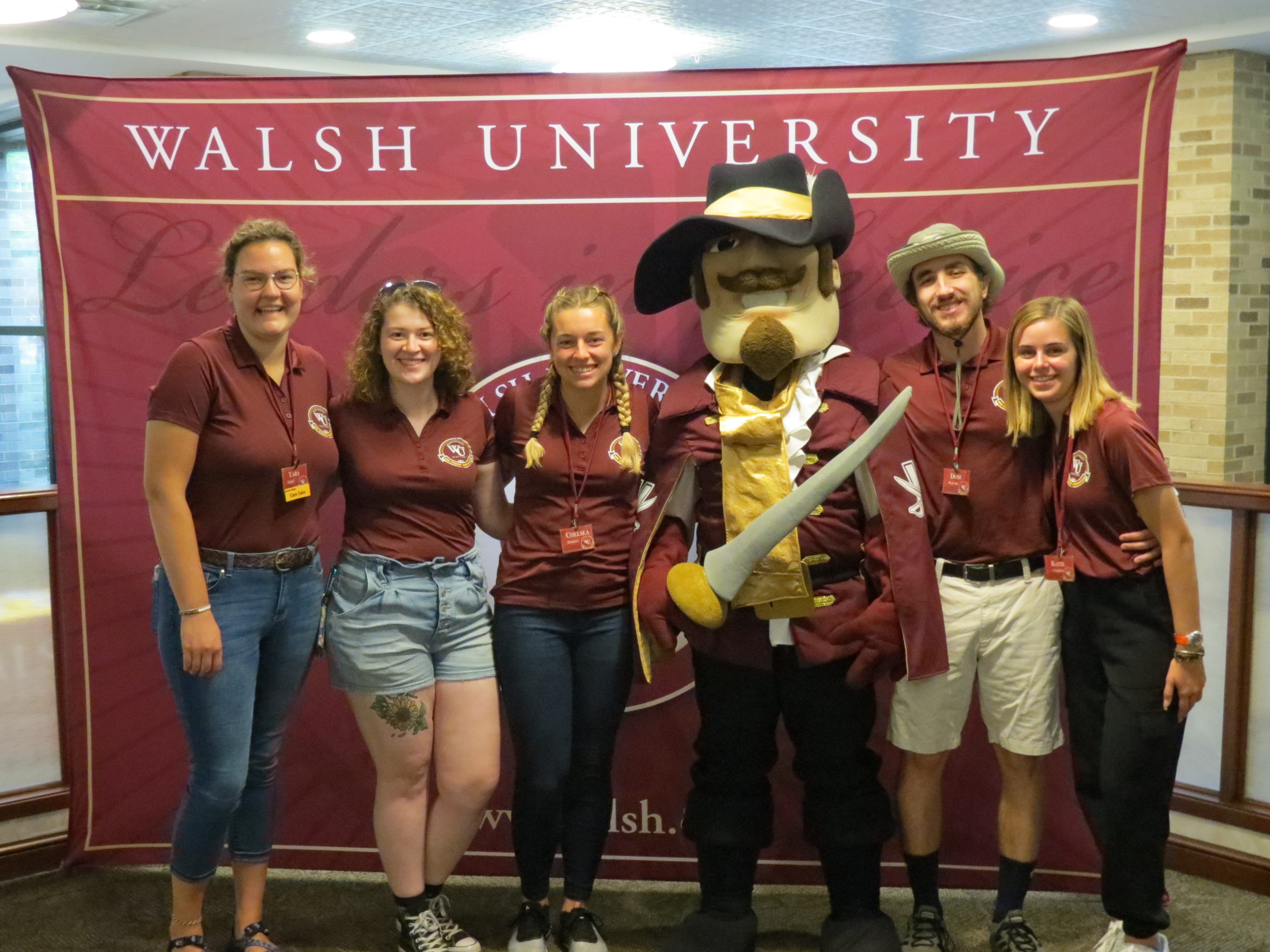 photo of a group of student orientation leaders and Sir Walter in front of a Walsh photo backdrop