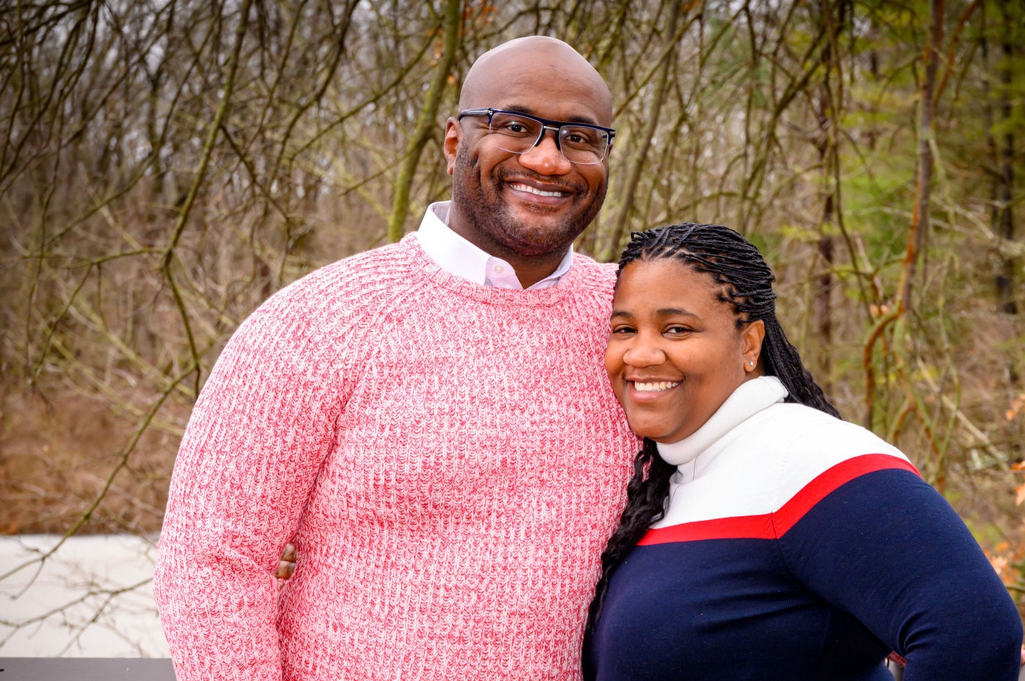 A cheerful couple posing together outdoors, dressed in cozy sweaters with a blurred natural background.