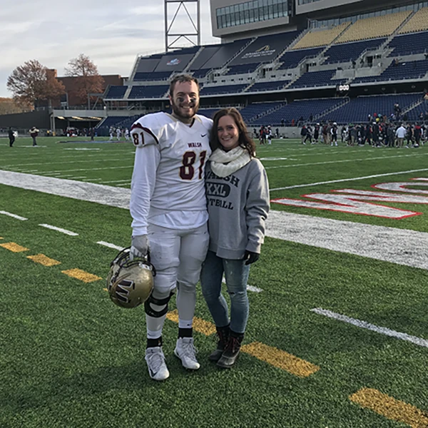 A football player in uniform poses with a woman on the field after a game.