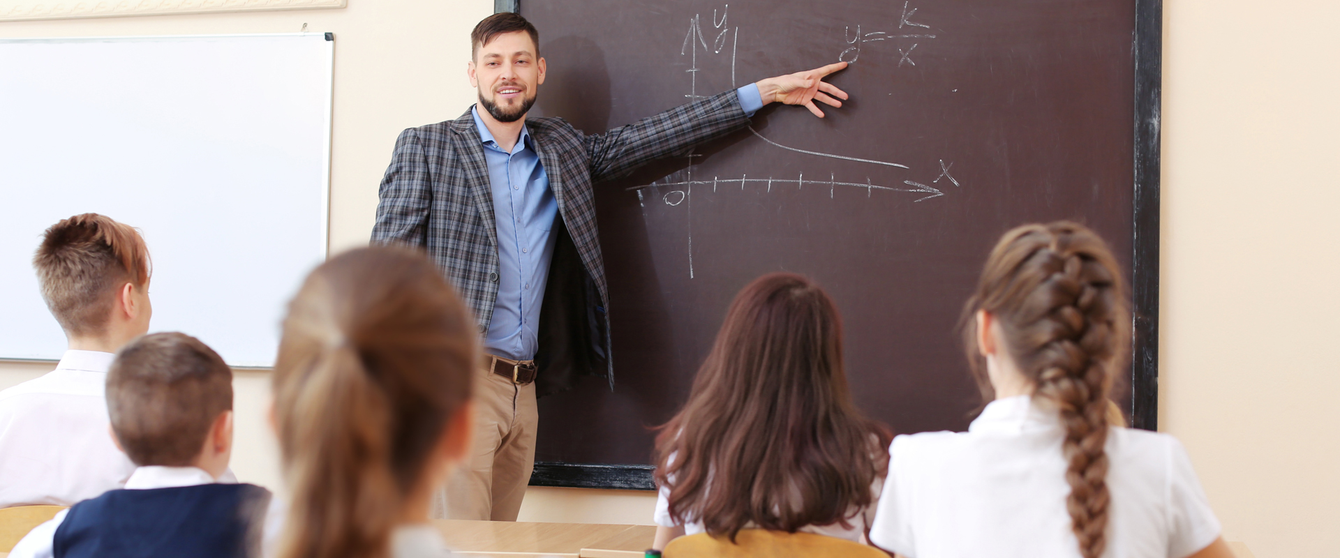 photo of a male teacher pointing at a blackboard in front of a class