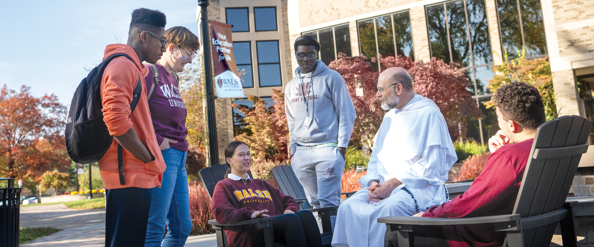 photo of a group of students and the University Chaplain seated by the Alumni fire pit