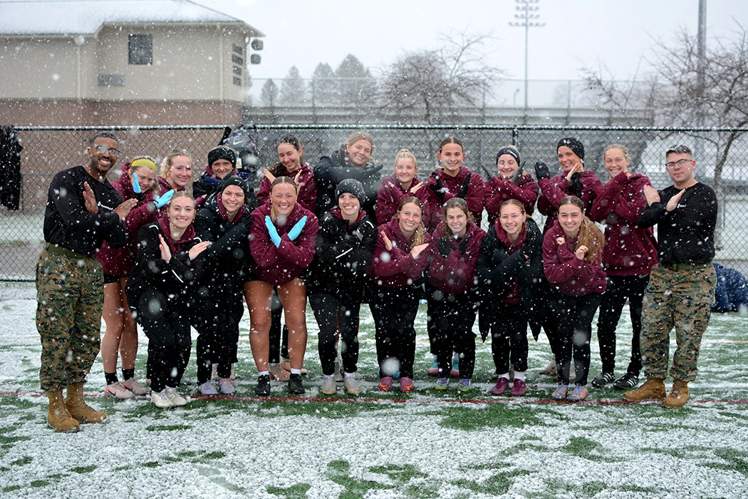 Women's Soccer team poses with Marines on a snowy field.