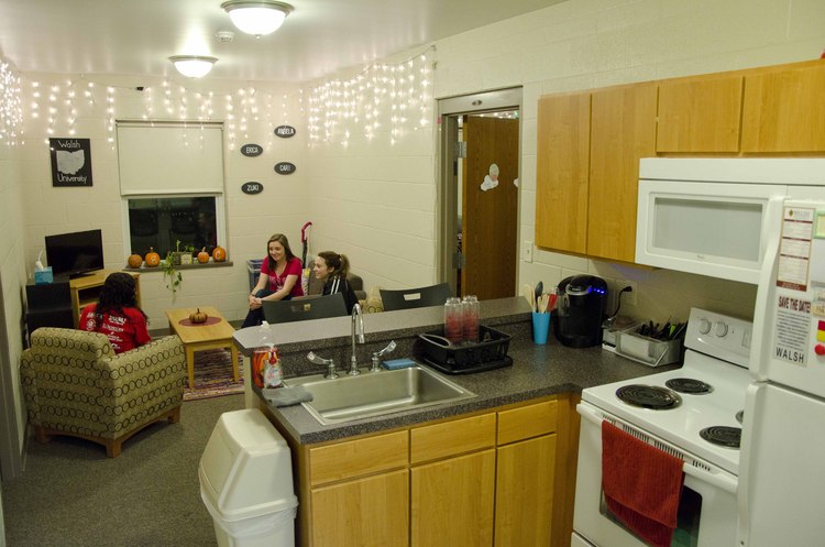 photo of The Commons kitchen amenities and three students sitting in the living area conversing