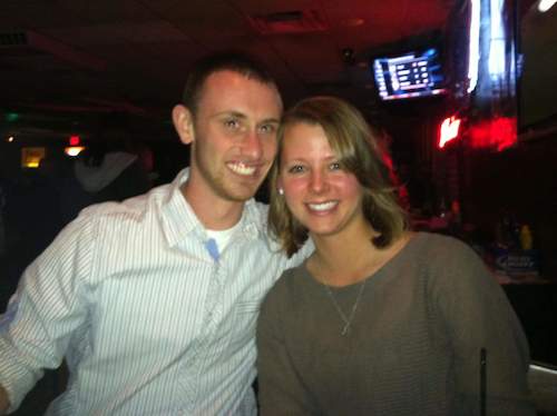 A couple smiling together at a social event in a bar setting.