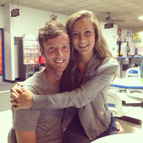 A young couple smiling and embracing in a casual bowling alley setting.